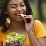 pretty-black-girl-eating-fresh-vegetable-salad-and-winking-at-green